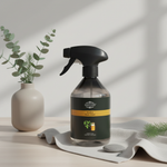 A dark plastic spray bottle with a black trigger sprayer and a dark green label reading 'Kingsbury' and 'Mead & Honey Balm' sits on a light fabric surface. A beige ceramic vase with eucalyptus stems and a small pine sprig are placed nearby in a softly lit interior setting.