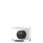 A white travel-sized candle with a label that reads 'PARKS Aromatherapy Baby Powder', housed in an elegant glass vessel with a silver base.