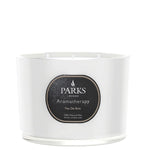 A white, glass-enclosed three-wick candle with a label that reads 'PARKS Aromatherapy Feu De Bois'.
