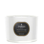 A white, glass vessel candle with a label that reads 'PARKS Aromatherapy Sandalwood & Ylang Ylang'. The candle is unlit and appears to be a luxury product.