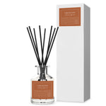 A clear glass diffuser bottle with black reeds and a label reading 'Firewood', alongside a white box with 'Firewood' and the seasons 'Autumn' & 'Winter' indicated on it.