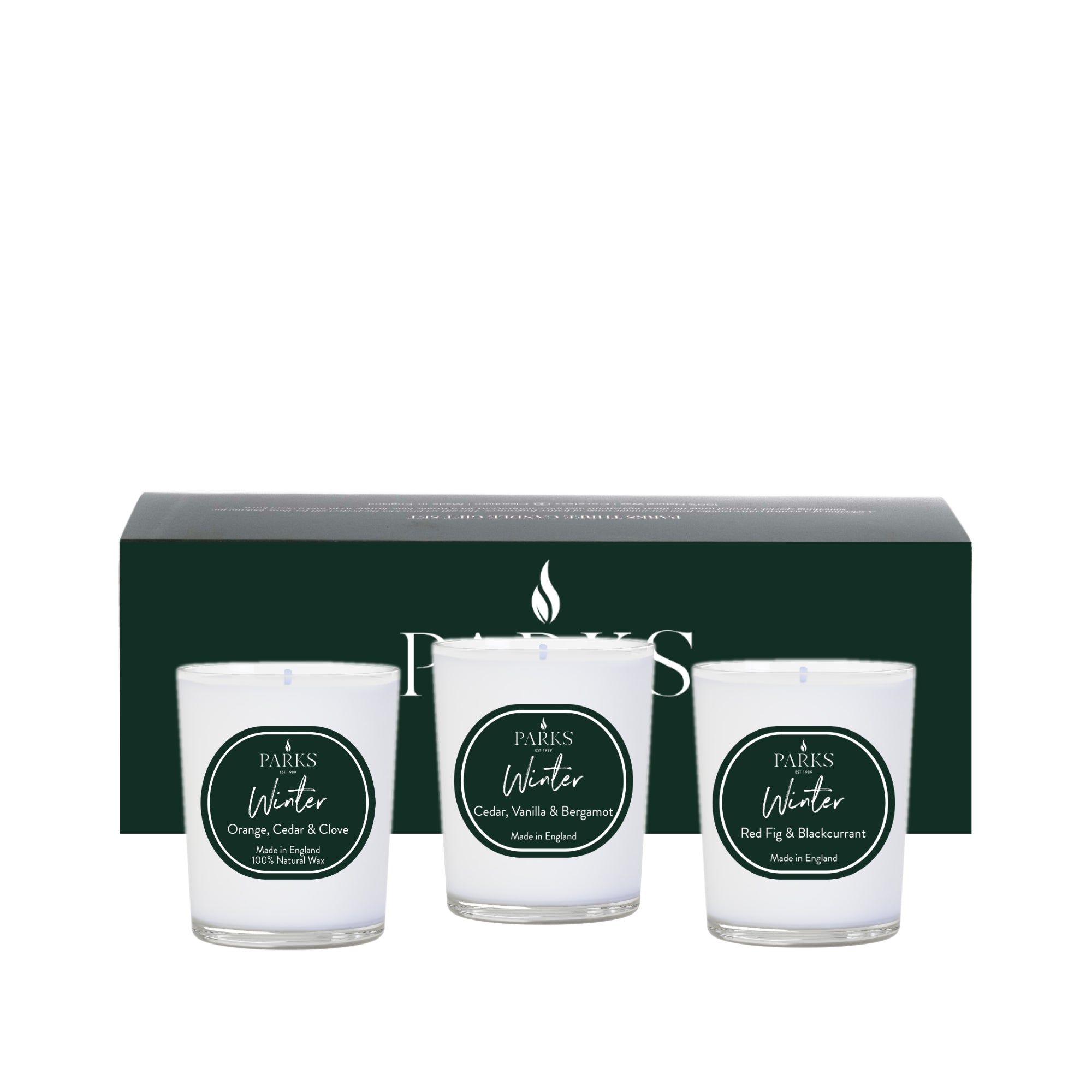 Three candles in white glass jars with green labels in front of a dark green box on a white background.